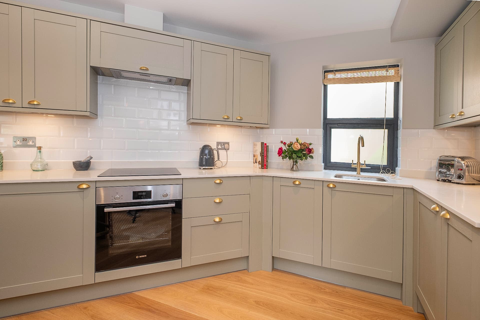 Sage grey kitchen with a tiled splashback, brass fittings and an integrated oven