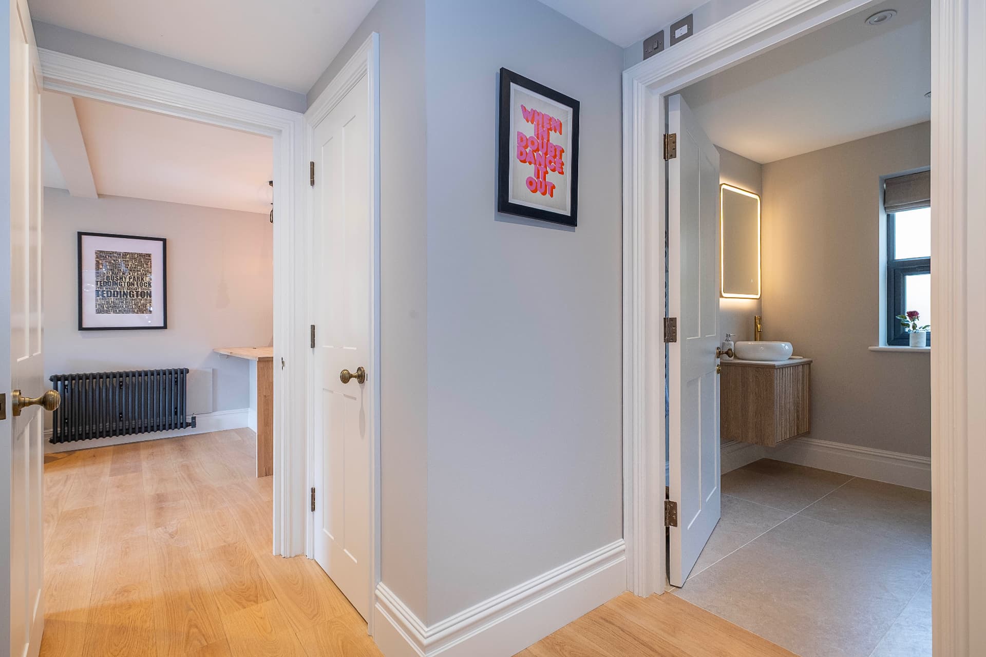 Hallway with white doors, framed artwork and timber flooring