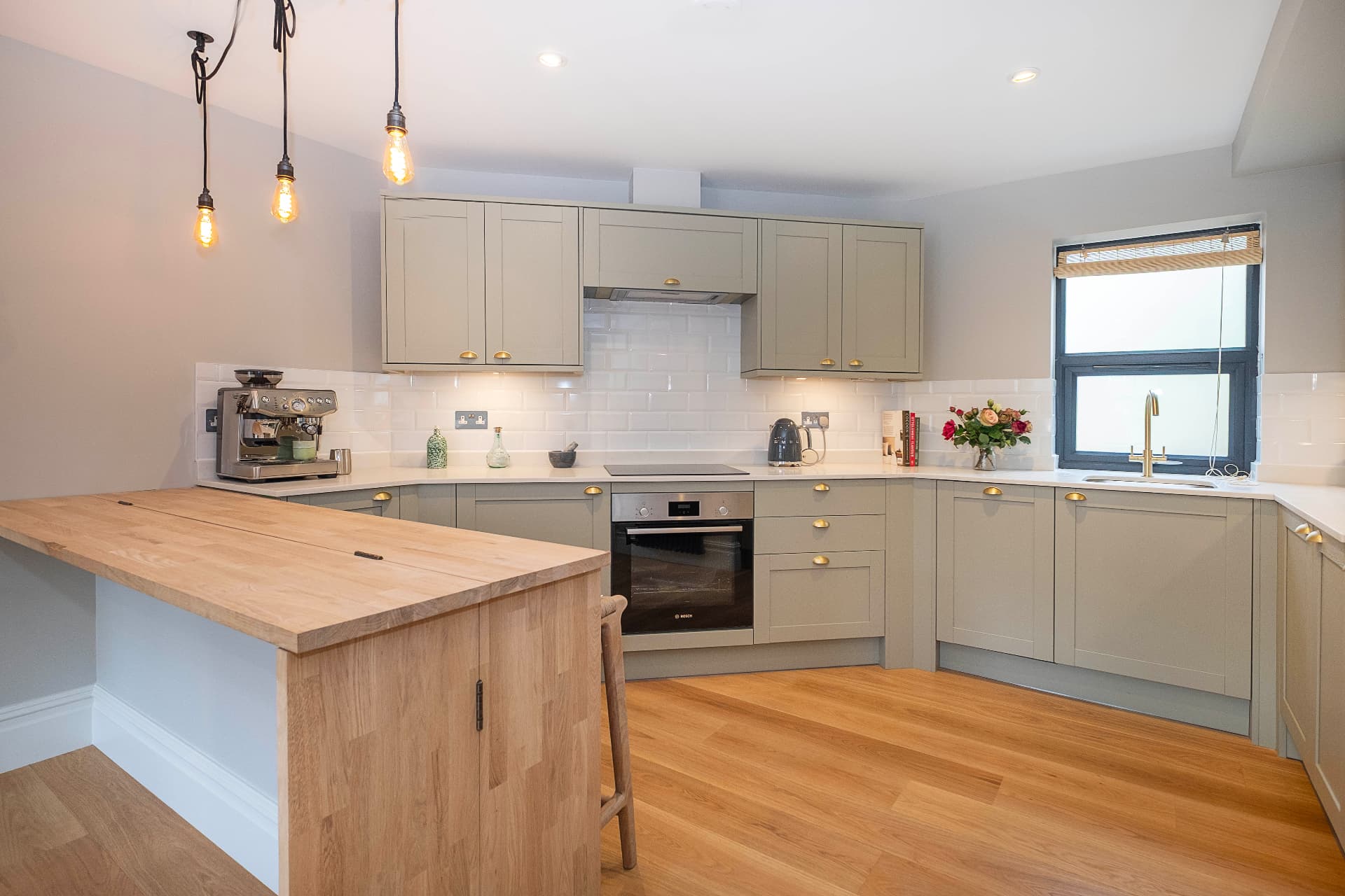 Sage grey kitchen with a wooden island, white subway tiles and integrated appliances