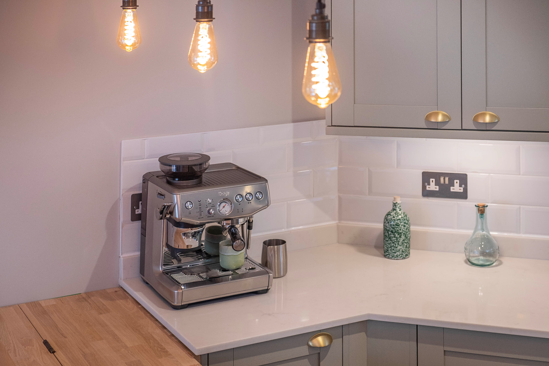 Kitchen detail with pendant bulbs, a coffee machine, white tiles and brass handles