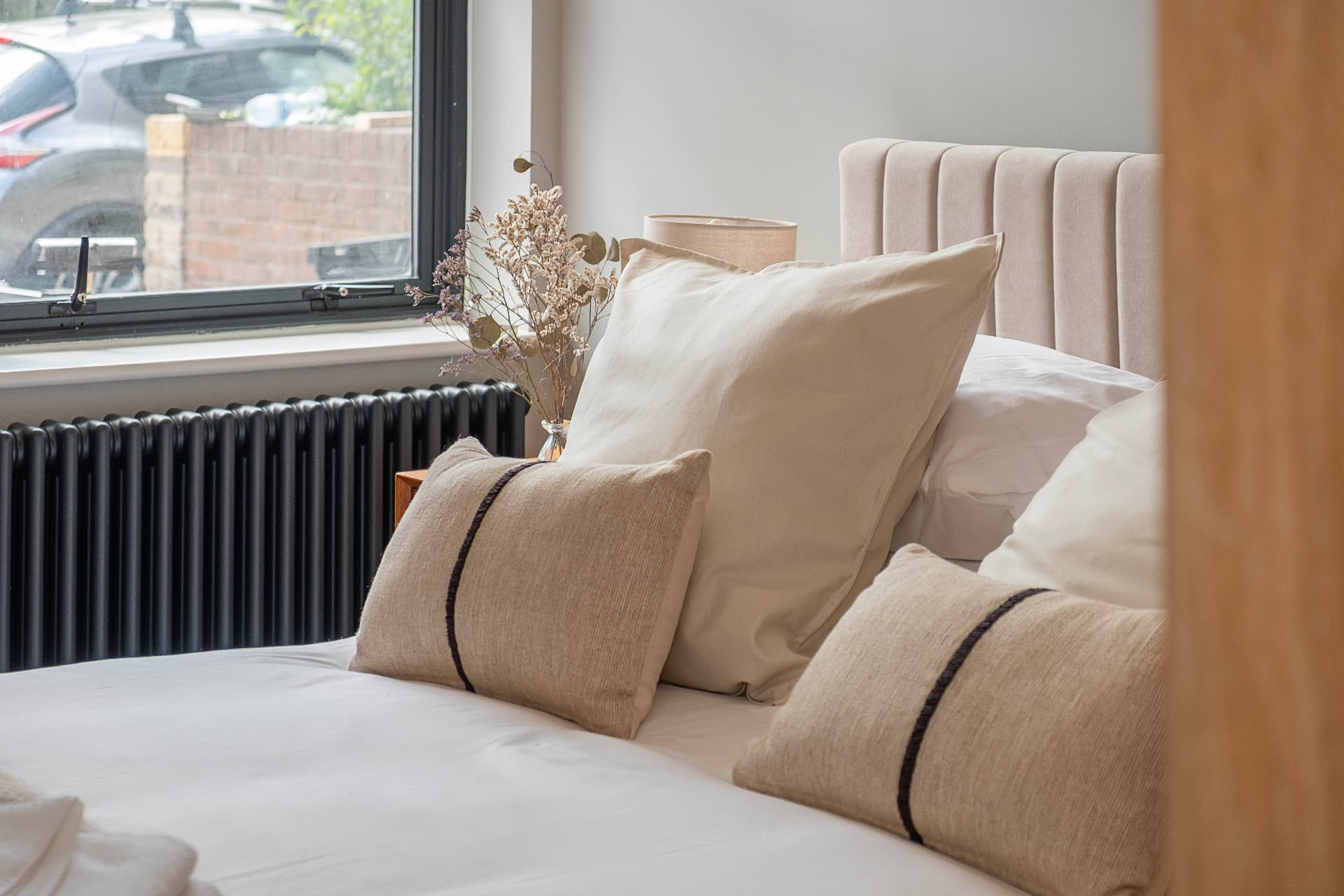 Close view of the bed, pillows, upholstered headboard and flowers by the window