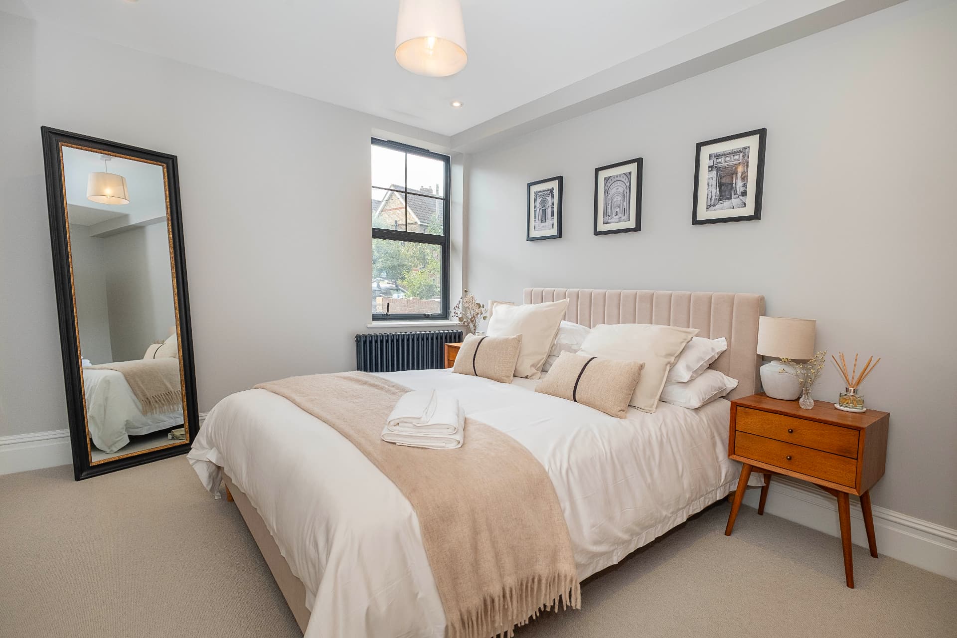Bedroom with a pale upholstered headboard, white bedding and a large window